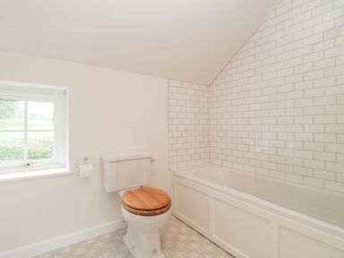 A bathroom with a toilet with wooden seat and a bathtub with tiled walls at Church View in Salisbury