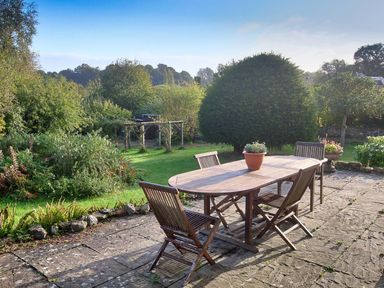 A garden patio with a wooden table and four chairs surrounded by plants and trees at Church View in Salisbury