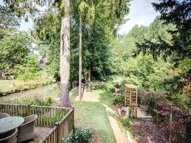 A garden with a wooden deck and wicker chairs overlooking a lawn and trees at Cider Press in Burford