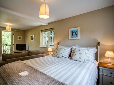 A bedroom with a striped bed and two cushions facing a sofa and TV at Cider Press in Burford