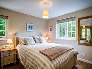 A bedroom with a striped bedspread bedside tables lamps and windows at Cider Press in Burford