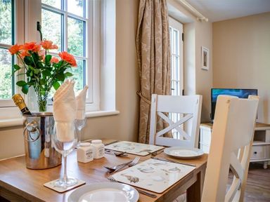 A dining table set for two with plates glasses and cutlery near a window with flowers in a vase and a champagne bottle in an ice bucket at Cider Press in Burford