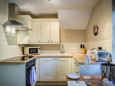 A kitchen with white cabinets a microwave a toaster a knife block and a table set with a plate and glass at Cider Press in Burford