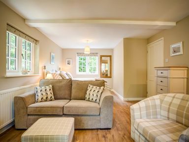 A living room with a beige sofa, armchair, ottoman, chest of drawers, and windows at Cider Press in Burford