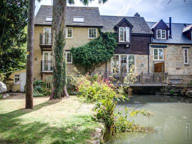 A stone and wood house with a garden and pond at Cider Press in Burford