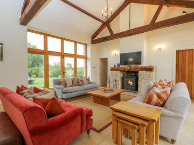 A living room with two sofas a coffee table a fireplace and a large window at Lower Farm Barn in Aston Near Bampton