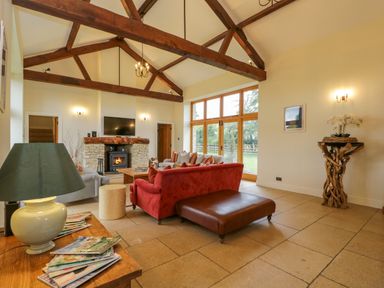 A living room with exposed wooden beams a fireplace and large windows at Lower Farm Barn Aston Near Bampton