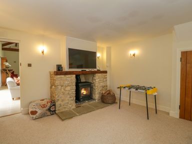 A room with a stone fireplace and wood burner a mounted television a foosball table and a cushioned seat by a doorway at Lower Farm Barn Aston Near Bampton