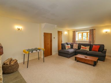 A living room with a gray sectional sofa a wooden coffee table a foosball table and a basket of firewood at Lower Farm Barn Aston Near Bampton