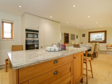 A kitchen with a wooden island with a marble countertop and a dining table with chairs at Lower Farm Barn in Aston Near Bampton