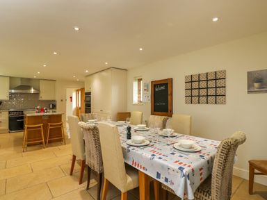 A dining area with a table set for six and a kitchen with an island and stove at Lower Farm Barn in Aston Near Bampton