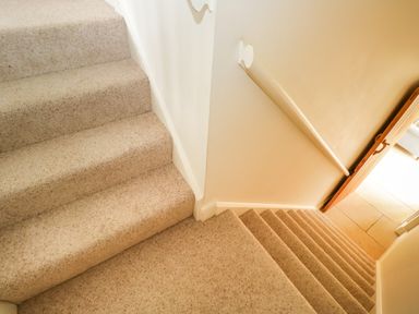 A carpeted stairwell with a handrail and an open door leading to a tiled floor at Lower Farm Barn in Aston Near Bampton