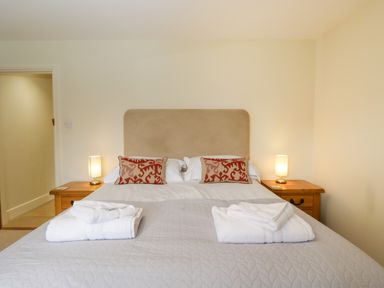 A bedroom with a double bed with white bedding brown headboard red patterned pillows two bedside tables with lamps at Lower Farm Barn in Aston Near Bampton