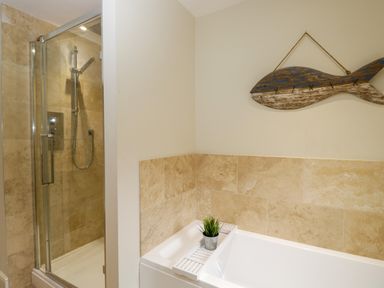 A bathroom with a glass shower enclosure and a bathtub with a plant on a tray and a wooden fish decoration on the wall at Lower Farm Barn Aston Near Bampton