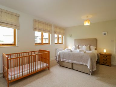 A bedroom with a double bed and a wooden baby crib near windows at Lower Farm Barn in Aston Near Bampton