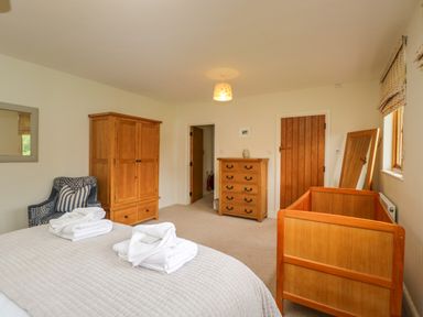 A bedroom with a bed, wooden wardrobe, chest of drawers, armchair and wooden crib at Lower Farm Barn Aston Near Bampton