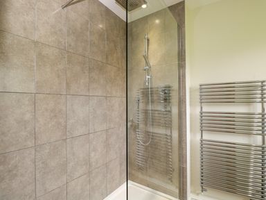 A bathroom with a tiled shower area and a chrome towel radiator at Lower Farm Barn in Aston Near Bampton