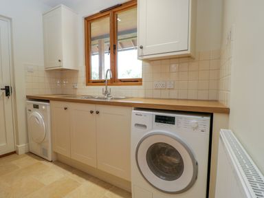 A utility room with a sink washing machine and dryer below wooden countertop at Lower Farm Barn Aston Near Bampton
