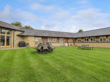 A grassy courtyard with stacked wicker chairs and a wooden picnic table at Lower Farm Barn in Aston Near Bampton