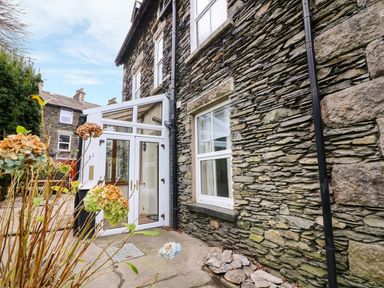 Stone exterior wall of a house with a white framed glass door and window with dried flowers in the foreground at Giddy Goose in Windermere