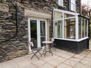 A stone exterior wall with glass double doors and a small patio with two chairs and a table at Giddy Goose in Windermere