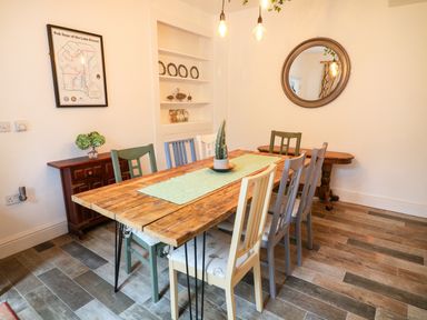 A dining room with a wooden table and six mixed color chairs a small sideboard with flowers a round mirror and a wall map at Giddy Goose in Windermere