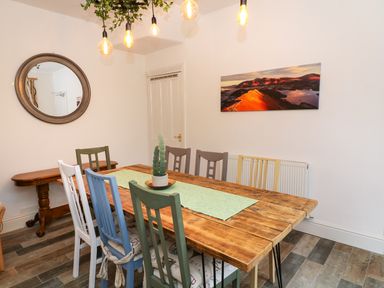 A dining room with a wooden table and mismatched colored chairs a round mirror on the wall and a landscape photo at Giddy Goose in Windermere