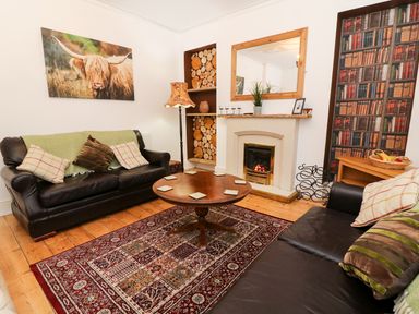 A living room with two leather sofas a round wooden coffee table a fireplace stacked wood and a bookshelf wallpaper at Giddy Goose in Windermere