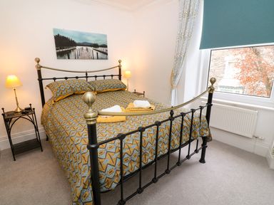 A bedroom with a metal bed frame a patterned bedspread two lamps on side tables and a window with curtains at Giddy Goose in Windermere