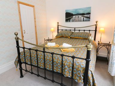 A bedroom with a metal bed frame patterned bedspread bedside tables and lamps at Giddy Goose in Windermere