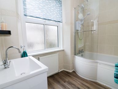 A bathroom with a sink a bathtub with shower and a window with a fish patterned blind at Giddy Goose in Windermere