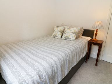 A bed with patterned pillows and a striped bedspread next to a wooden side table with a lamp at Giddy Goose in Windermere
