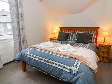 A bedroom with a double bed with blue patterned bedding two rolled towels and bedside tables with lamps at Giddy Goose in Windermere