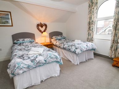 A bedroom with two single beds with patterned bedding a bedside table with a lamp and a heart-shaped wall decoration at Giddy Goose in Windermere
