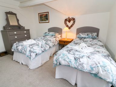 A bedroom with two single beds a dresser and a bedside table with a lamp at Giddy Goose in Windermere