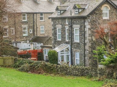 Stone houses with slate roofs behind a stone wall and green lawn at Giddy Goose in Windermere