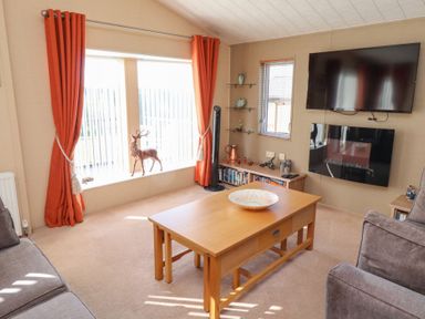 A living room with a wooden coffee table sofa orange curtains a mounted television and a fireplace at Percy Wood Country Park in Swarland