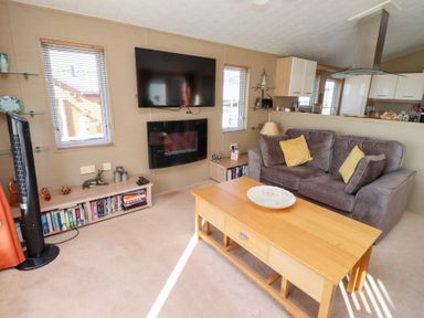 A living room with a gray couch yellow pillows wooden coffee table mounted TV and fireplace at Percy Wood Country Park Swarland