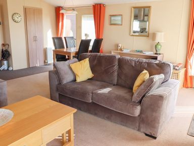 A living room with a gray sofa with yellow pillows a wooden coffee table a dining table with black chairs and orange curtains at Percy Wood Country Park in Swarland
