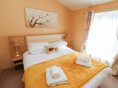 A bedroom with a double bed orange blanket bedside lamps and a painting above the headboard at Percy Wood Country Park Swarland