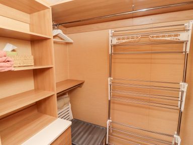 A storage room with wooden shelves towels tissue box hangers a folding drying rack and a plastic container at Percy Wood Country Park Swarland