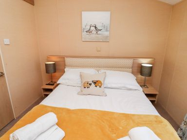 A bedroom with a bed, two bedside tables with lamps, a picture on the wall, and folded towels on the bed at Percy Wood Country Park in Swarland