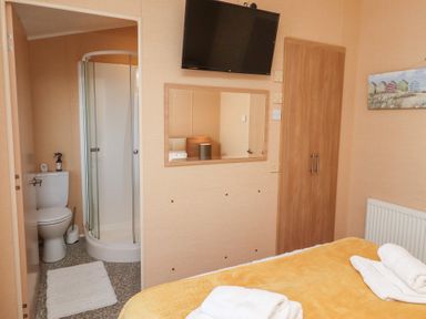 A bedroom with a bed with folded towels a wall-mounted tv a wardrobe and an en suite bathroom with a shower at Percy Wood Country Park Swarland