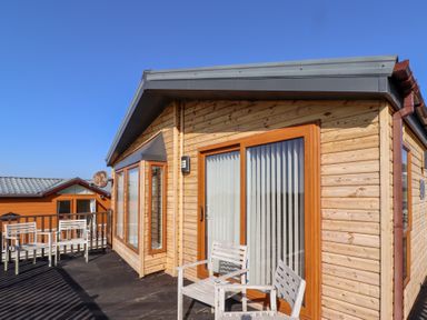 Wooden exterior of a cabin with a deck and white chairs at Percy Wood Country Park in Swarland