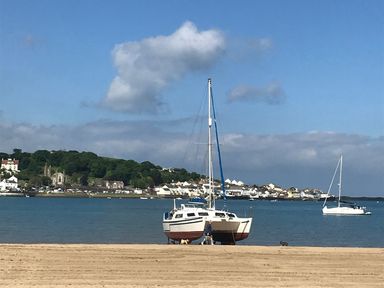 A sandy beach with two boats on shore and water with houses and trees in the background at Beach Retreat in Instow