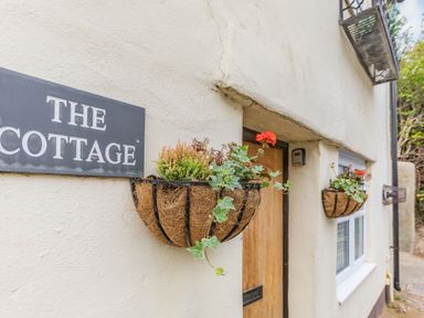 The exterior of a cottage with flower baskets and a sign that reads The Cottage at Beach Retreat in Instow