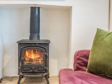 A black wood burning stove with fire inside next to a purple sofa with a green cushion at Beach Retreat in Instow