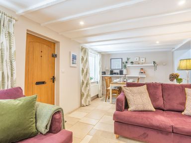 A living room with purple sofas green pillows wooden door and dining table with chairs at Beach Retreat in Instow