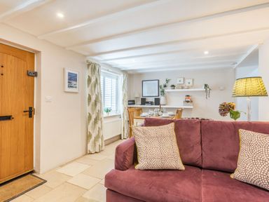 A living room with a purple sofa and dining table near a window with patterned curtains at Beach Retreat in Instow