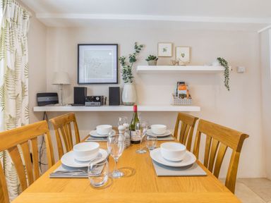 A dining room with a wooden table set for four and shelves with plants and decorations at Beach Retreat in Instow